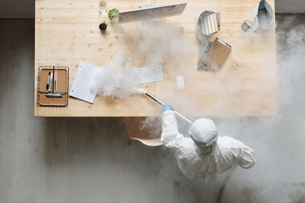 services-02 An individual disinfects a workspace using fumigation, wearing full protective gear for safety.